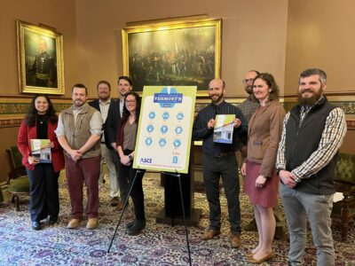 A group of people are standing next to a a sign presenting Vermont's Report Card showcasing American Infrastructure.